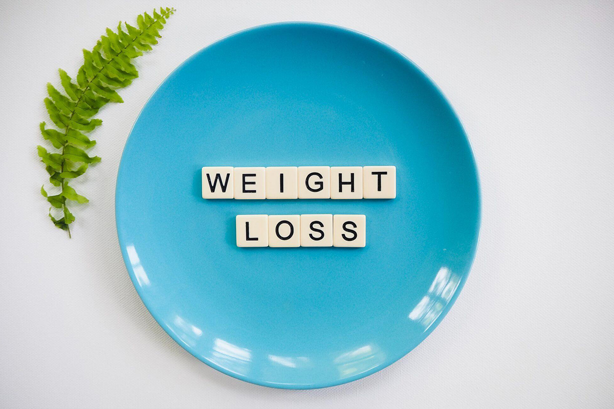Blue plate with scrabble tiles spelling weight loss, representing the distinction between dieting and liposuction goals