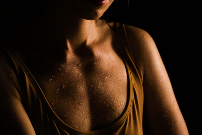 Close-up of a woman’s chest with water droplets, symbolizing natural body contours and breast enhancement options