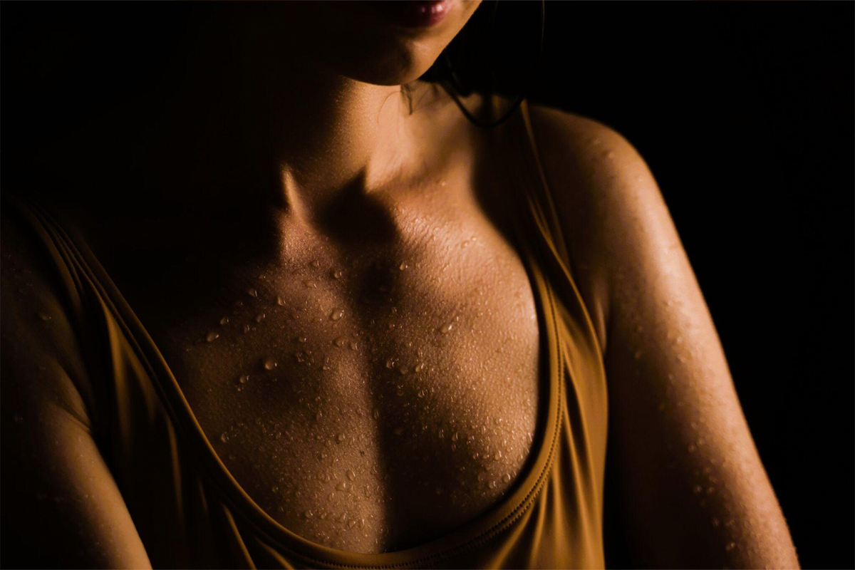 Close-up of a woman’s chest with water droplets, symbolizing natural body contours and breast enhancement options