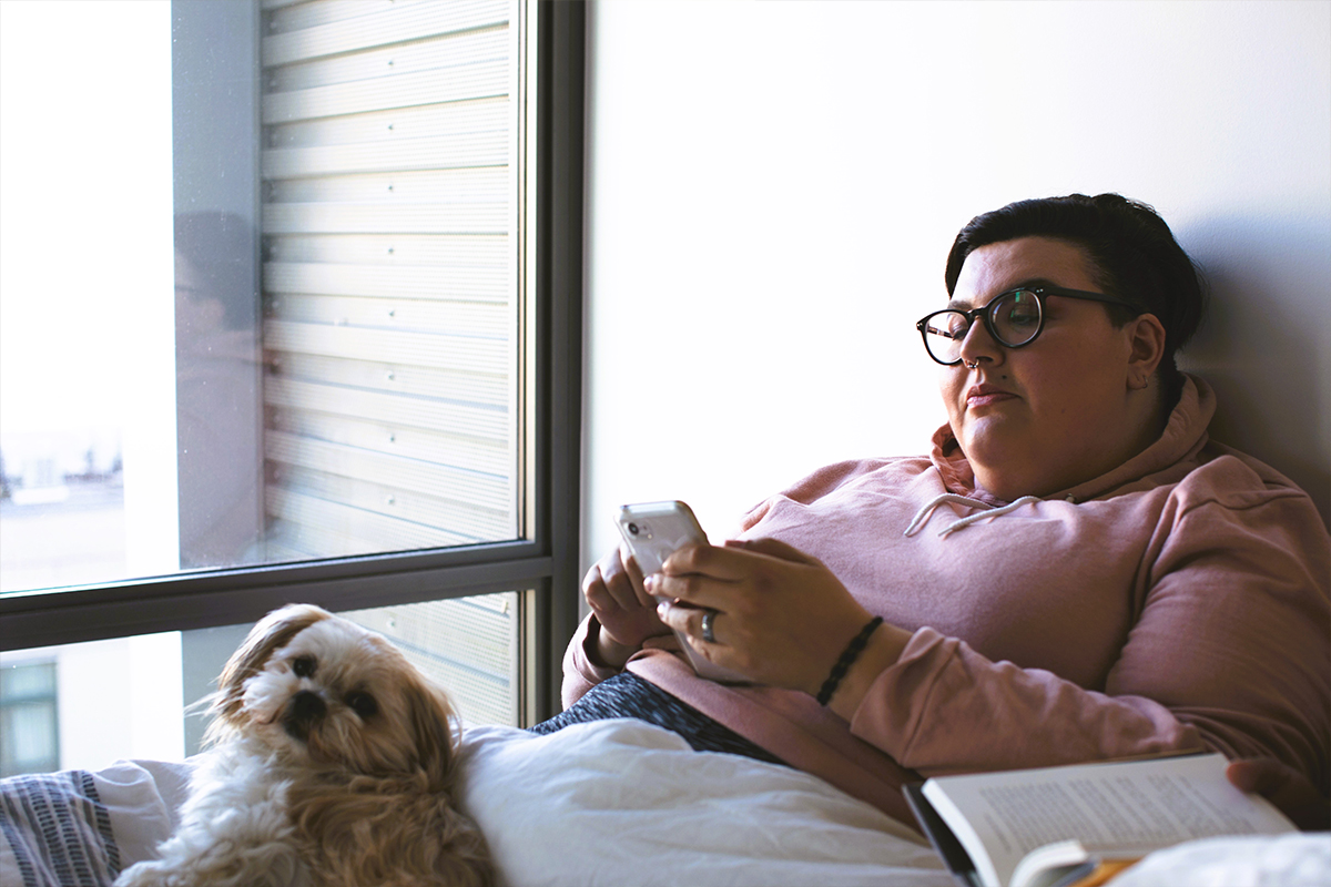 Person relaxing at home with phone and dog, preparing mentally and physically before liposuction surgery