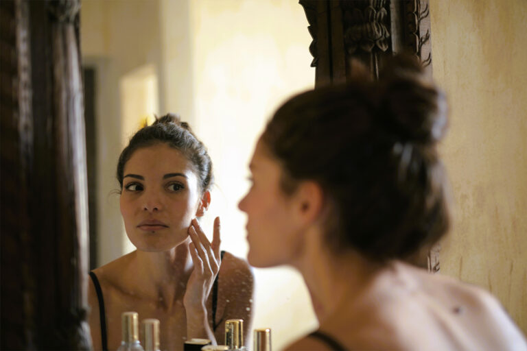 Woman examining her neck and chin in mirror, considering skin firmness and cosmetic surgery options.