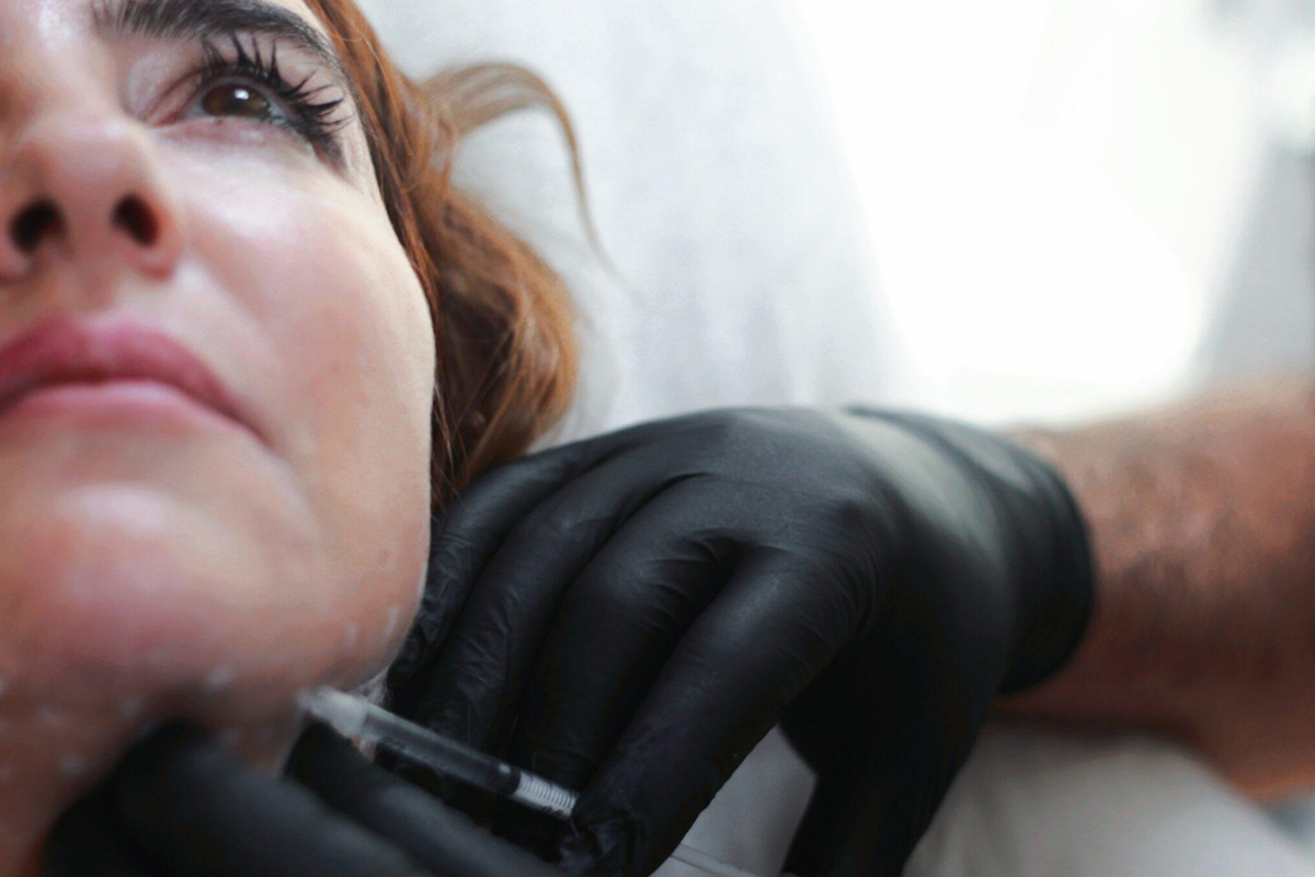 Close-up of woman receiving dermal filler injection under the chin from gloved professional for facial contouring.