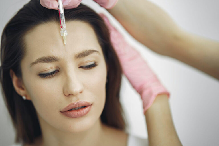 Woman receiving a forehead filler injection from a professional in pink gloves, aiming for subtle, natural-looking results.