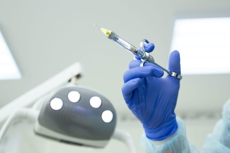 Gloved medical professional holding a syringe under bright surgical lights, preparing for a safe cosmetic procedure.