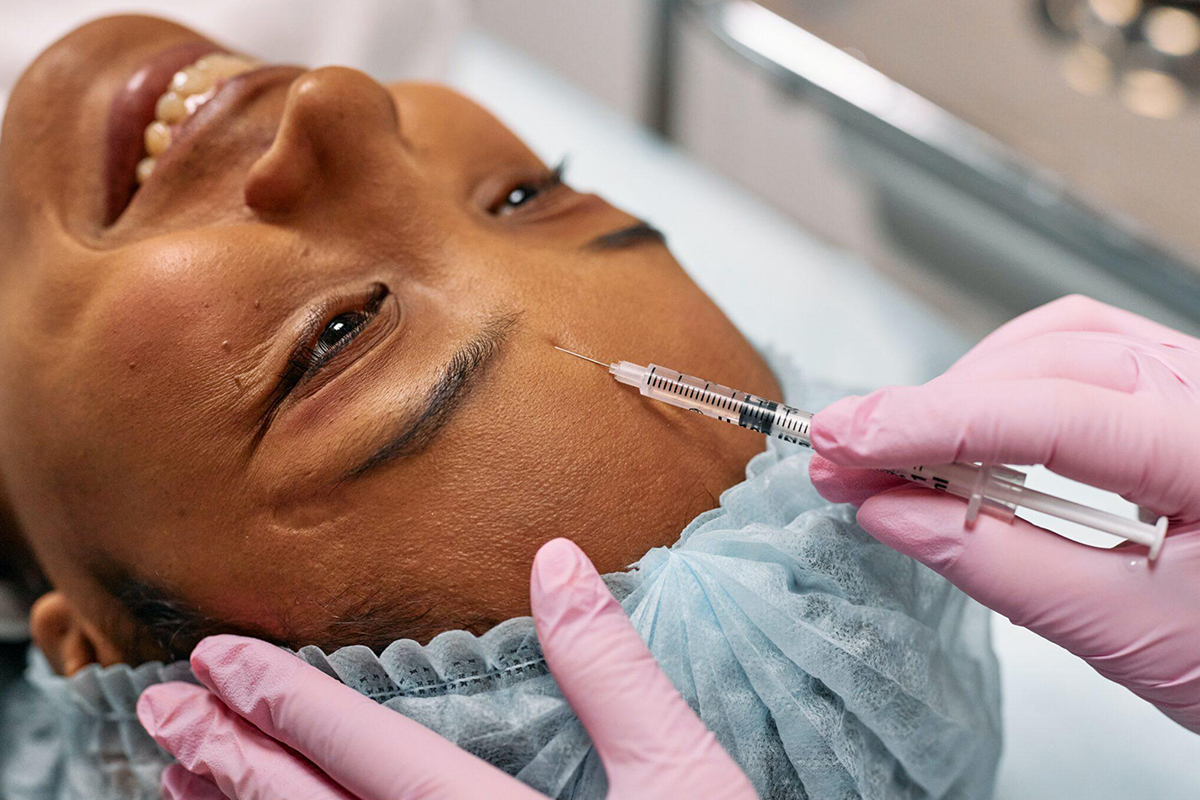 Smiling woman receiving a Botox injection in the forehead, representing a non-invasive option to improve appearance without surgery.