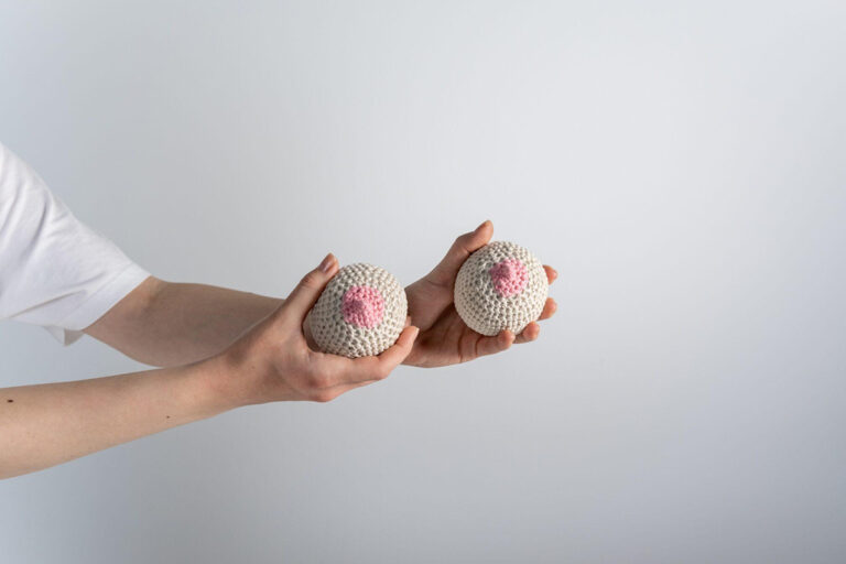 Person holding two knitted breast models, illustrating the process of exploring breast implant sizes for augmentation.