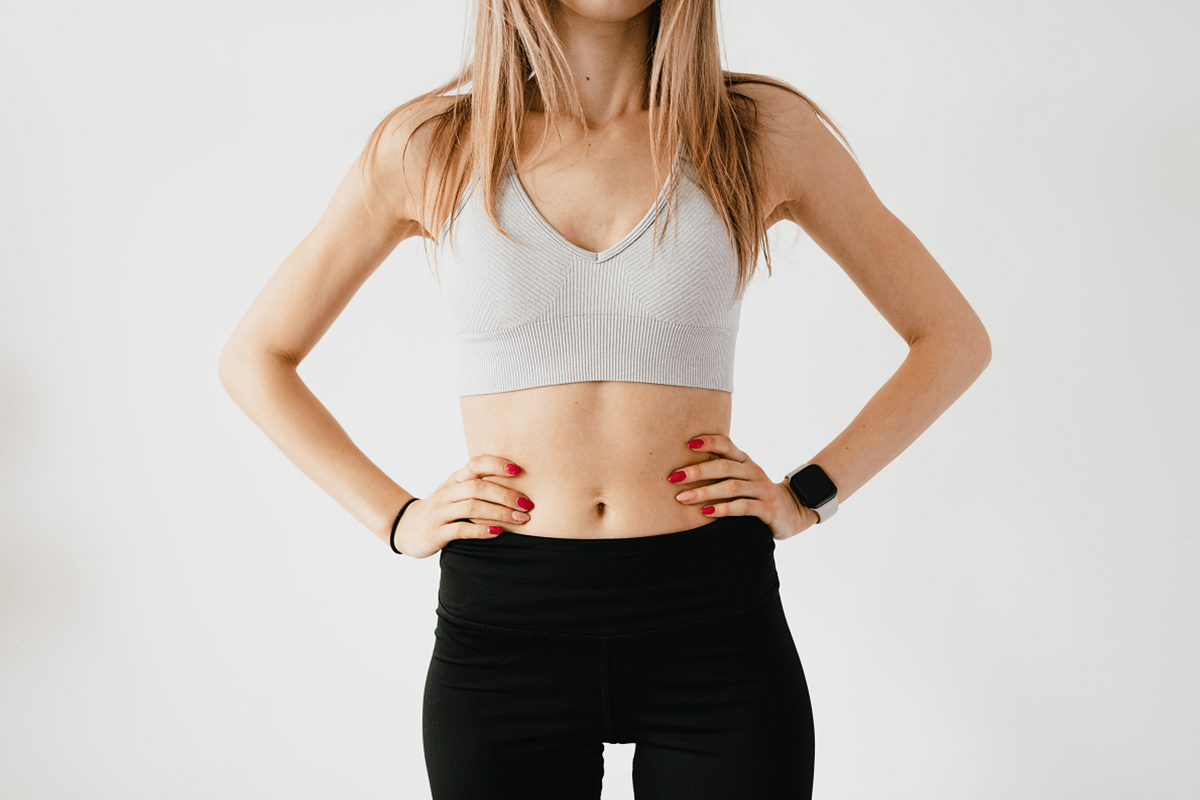 Fit woman in workout clothes showing toned midsection, illustrating the body contouring benefits of liposuction.