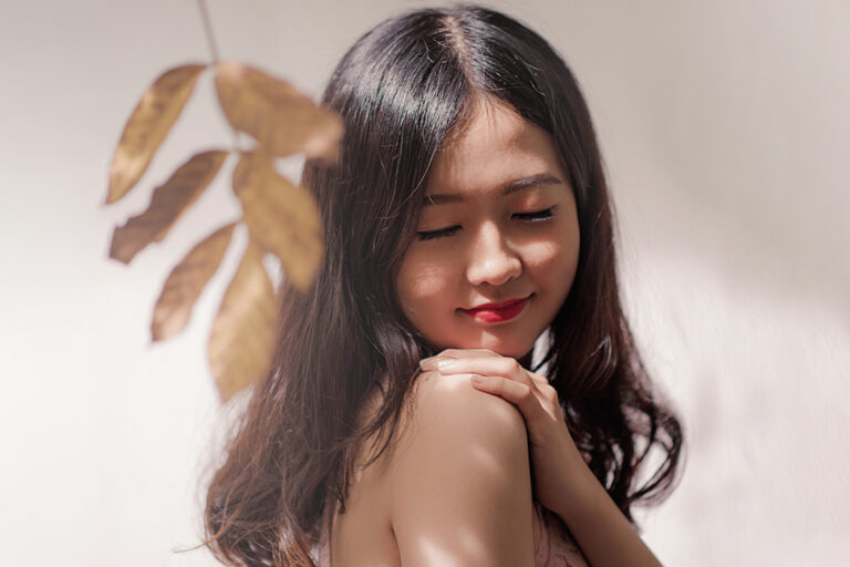 Peaceful woman touching her shoulder in soft light, symbolizing confidence and healing after breast lift surgery.