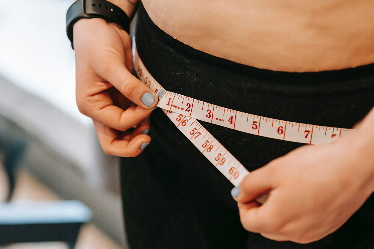 Person measuring waist with tape, symbolizing documentation and assessment for insurance-covered breast reduction surgery.