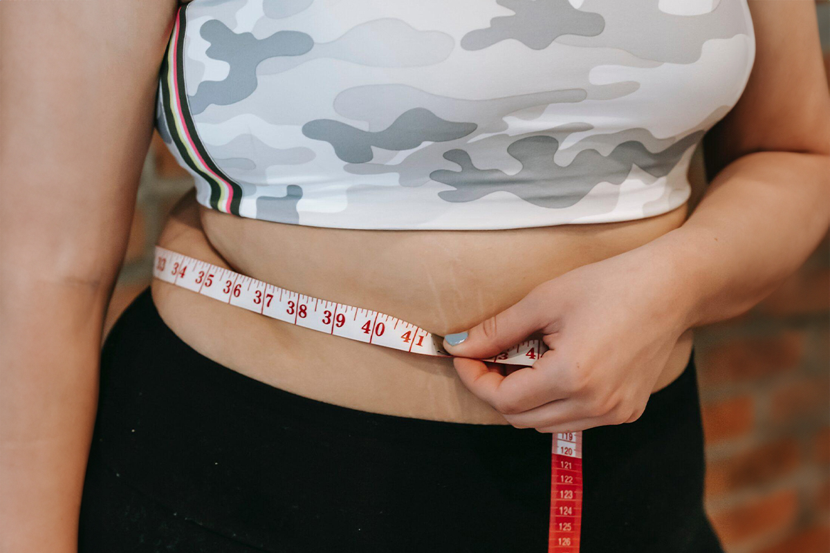 Woman measuring her waist with tape, representing evaluation for plastic surgery procedures like tummy tuck or liposuction.