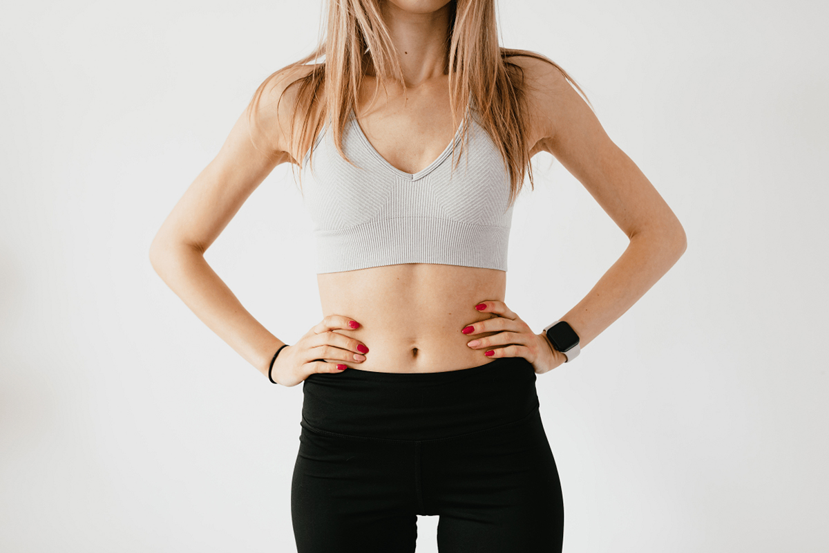 Woman in workout clothes with flat stomach, highlighting results from tummy tuck vs liposuction cosmetic procedures.