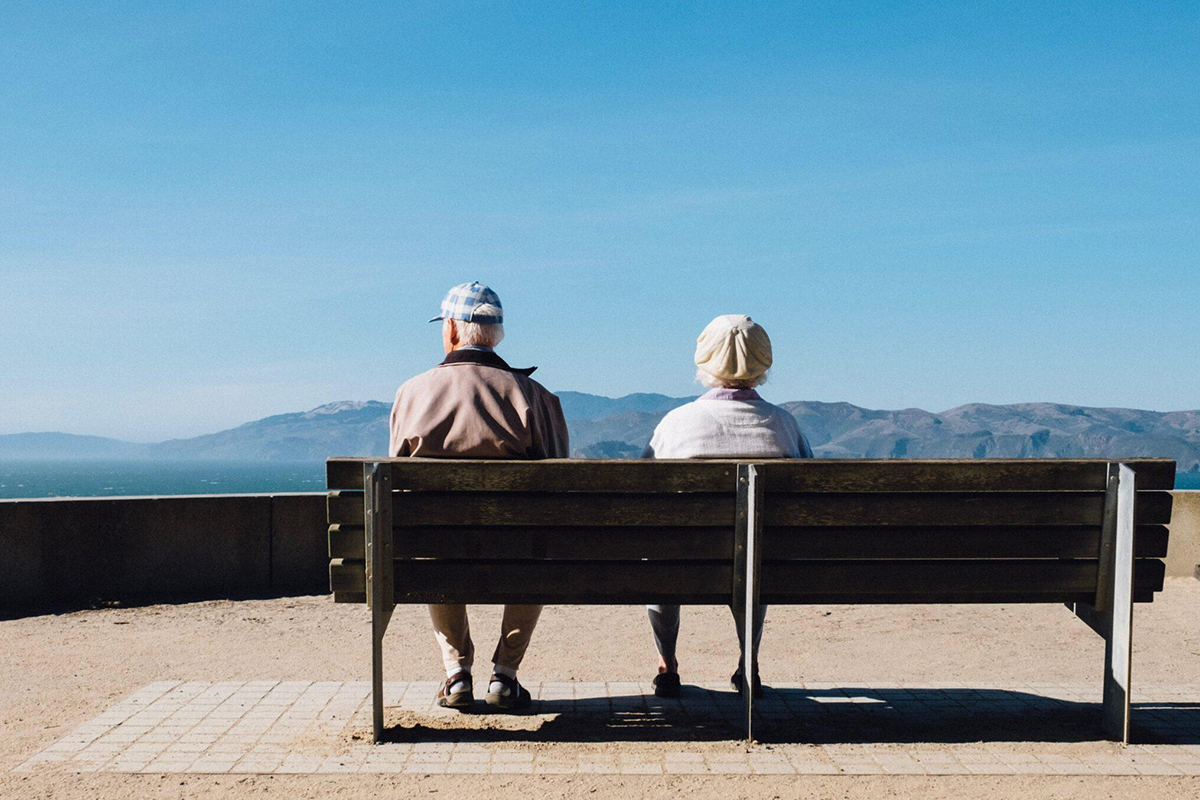 Senior couple sitting on bench facing mountains, representing peaceful recovery time after blepharoplasty surgery.