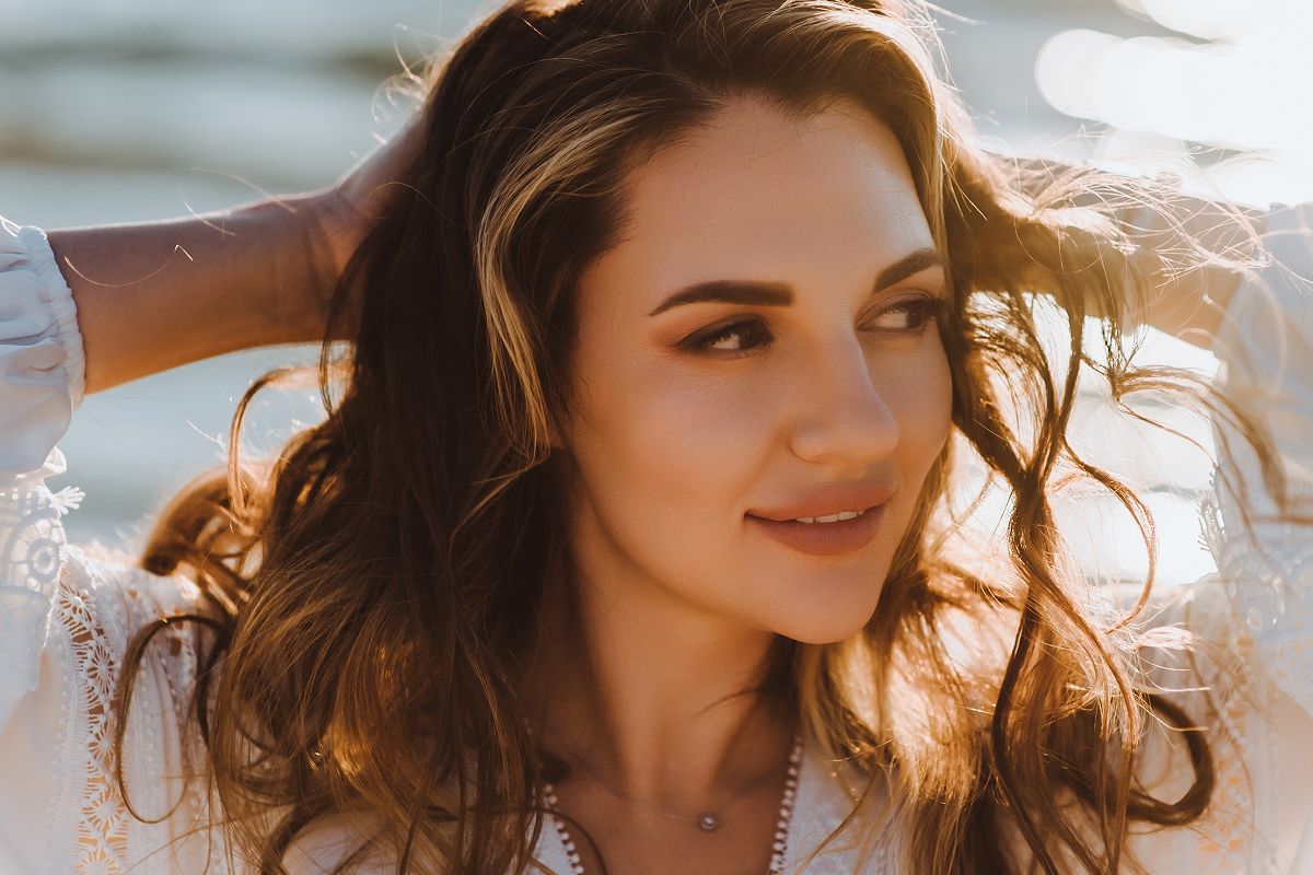 Woman with smooth, symmetrical nose smiling outdoors after non-surgical rhinoplasty