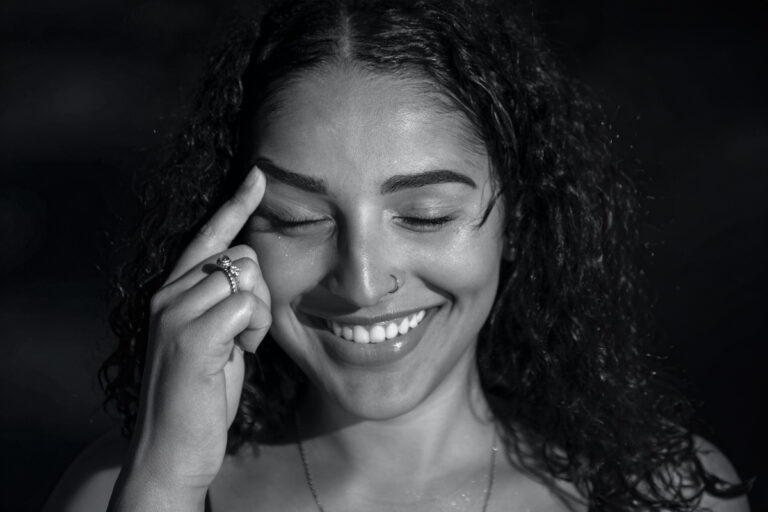 Smiling woman touching her eyebrow, representing youthful appearance after upper eyelid lift surgery