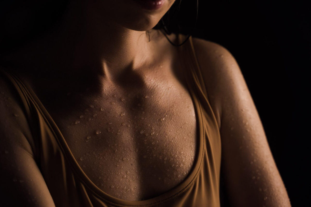 Close-up of a woman's chest and shoulders with water droplets on her skin, representing breast implant and augmentation options