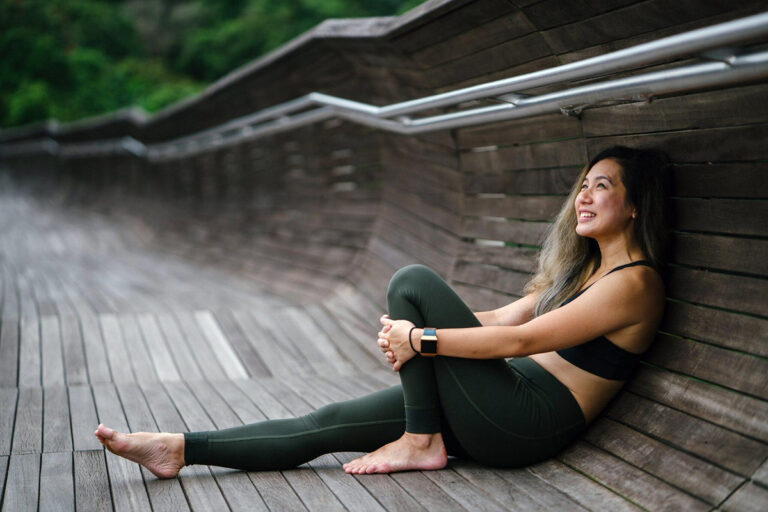Woman in activewear smiling and sitting on a wooden boardwalk, symbolizing post-liposuction recovery