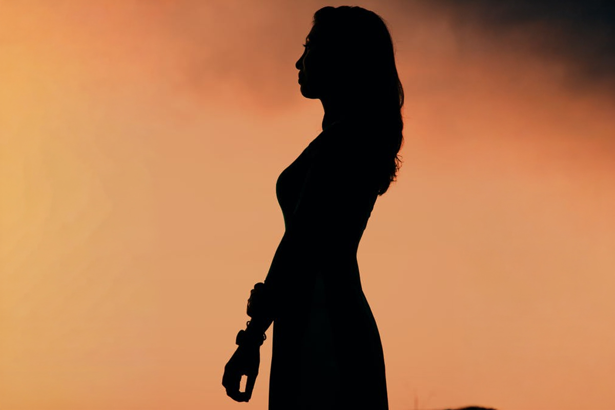 Silhouette of a woman standing against a sunset background, representing body confidence and breast lift procedure awareness.