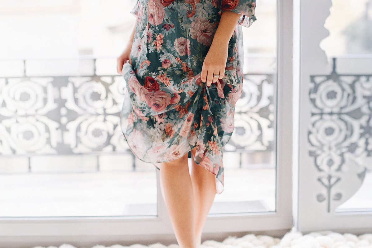 Woman in floral dress holding fabric near stomach, symbolizing improved abdominal contour from cosmetic procedures