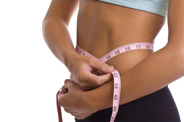Closeup of fit woman measuring slim waist with pink tape, showing effective results of liposuction fat removal