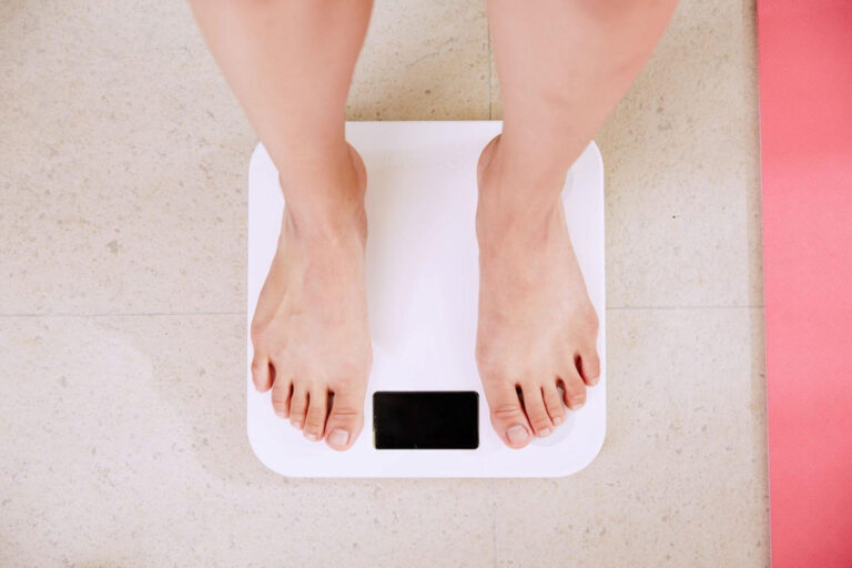 Barefoot person standing on white bathroom scale, representing realistic weight loss expectations after liposuction