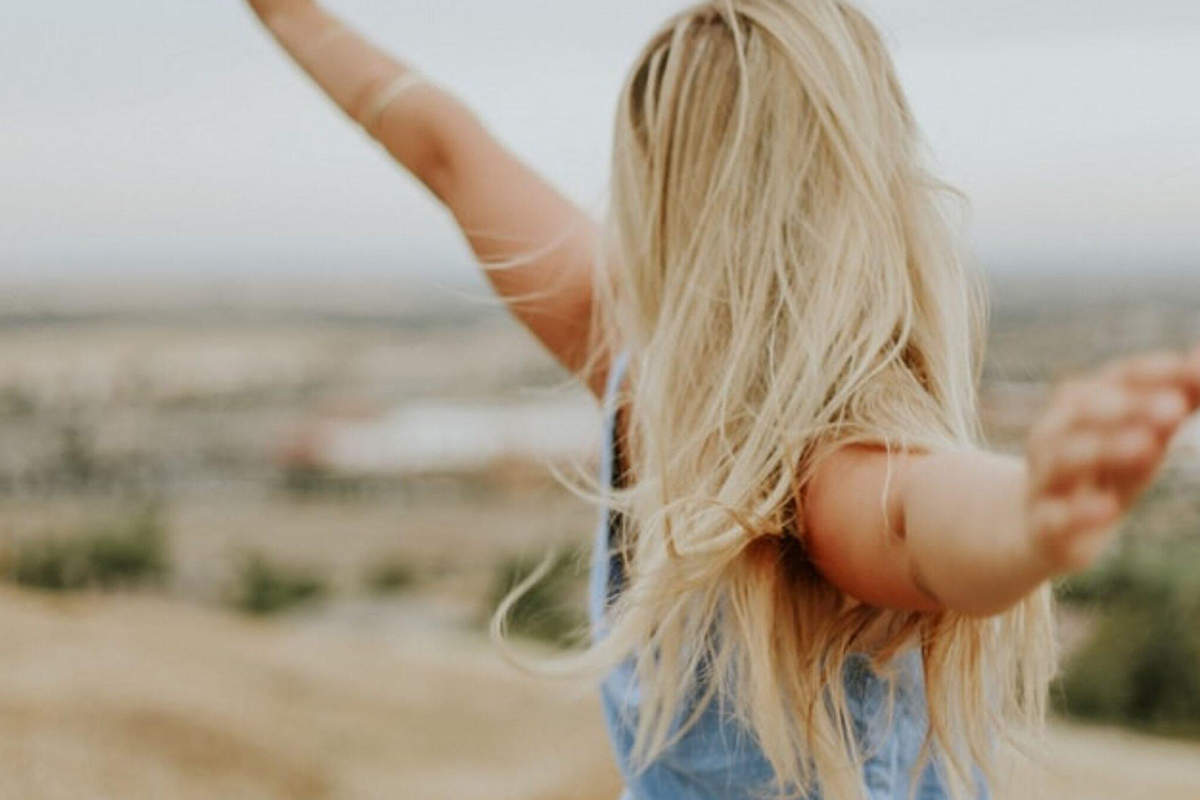 Blonde woman with arms outstretched outdoors, symbolizing confidence and freedom after arm lift surgery for flabby arms.
