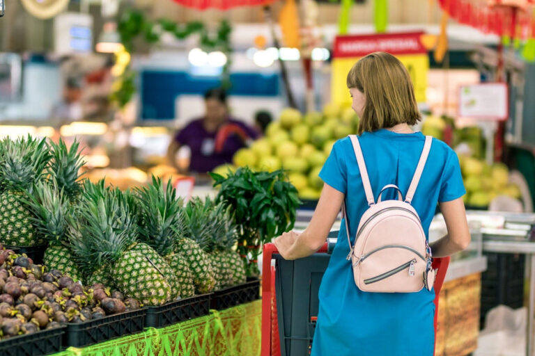 Woman in blue dress shopping for fresh produce like pineapples, symbolizing healthy nutrition before cosmetic surgery