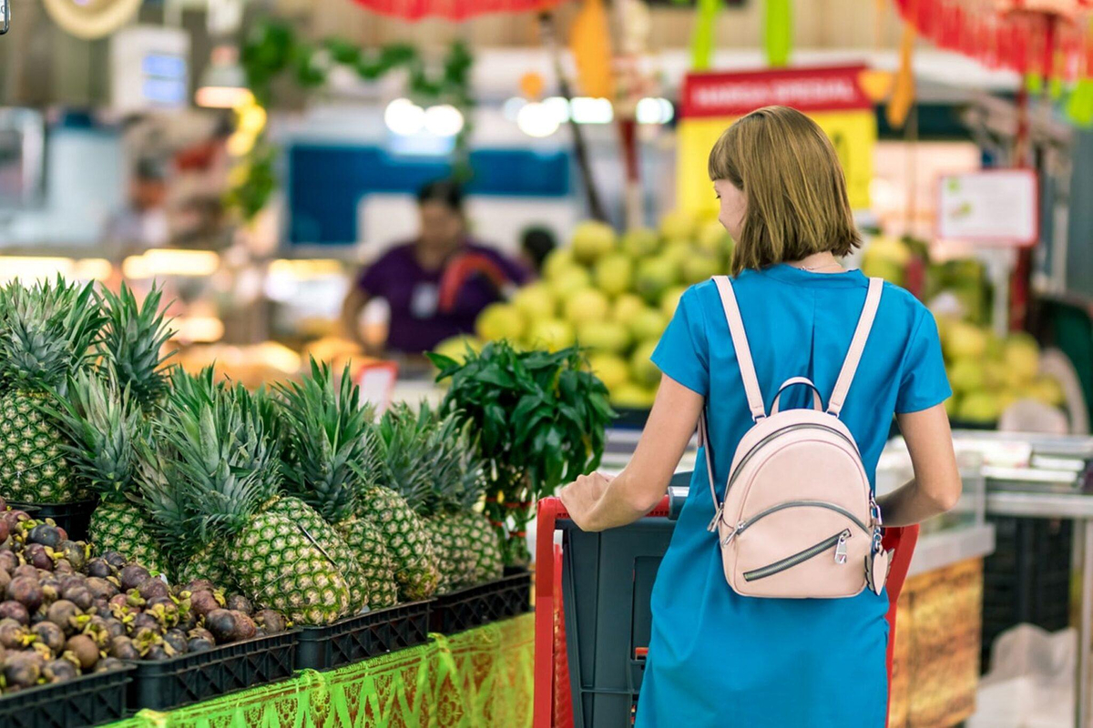 Woman in blue dress shopping for fresh produce like pineapples, symbolizing healthy nutrition before cosmetic surgery