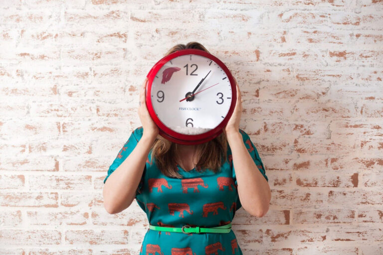 Woman holding red clock in front of face, symbolizing the typical two-hour duration of blepharoplasty surgery
