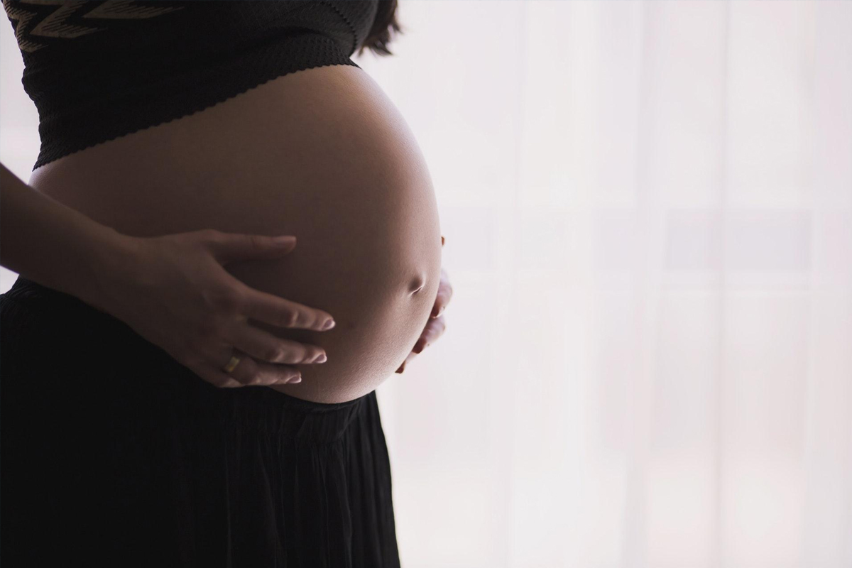 Closeup of pregnant woman holding belly, representing body changes before exercise recovery after a mommy makeover