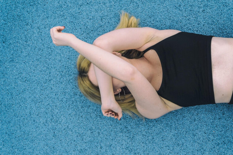 Woman lying on blue surface with arms raised, symbolizing self-consciousness and need for flabby arm plastic surgery solution
