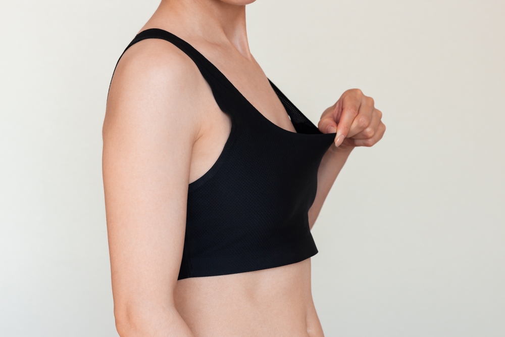 Woman assessing breast firmness in black top, illustrating alternative breast procedures after weight loss such as lift or revision.