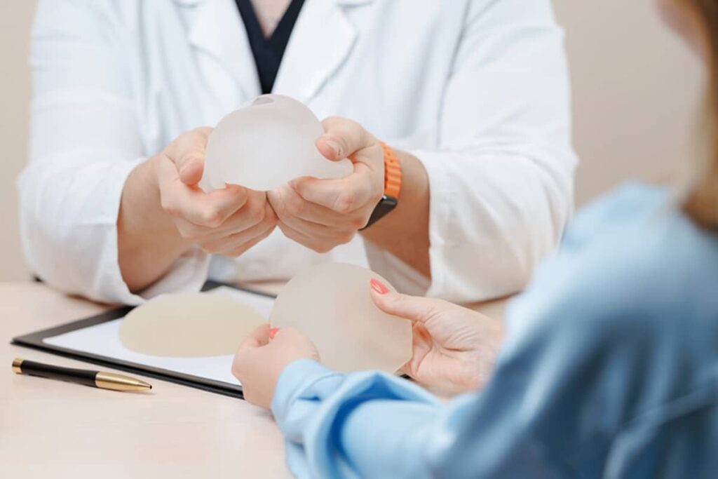 A plastic surgeon in a white coat showing different breast implant options to a patient during a medical consultation.