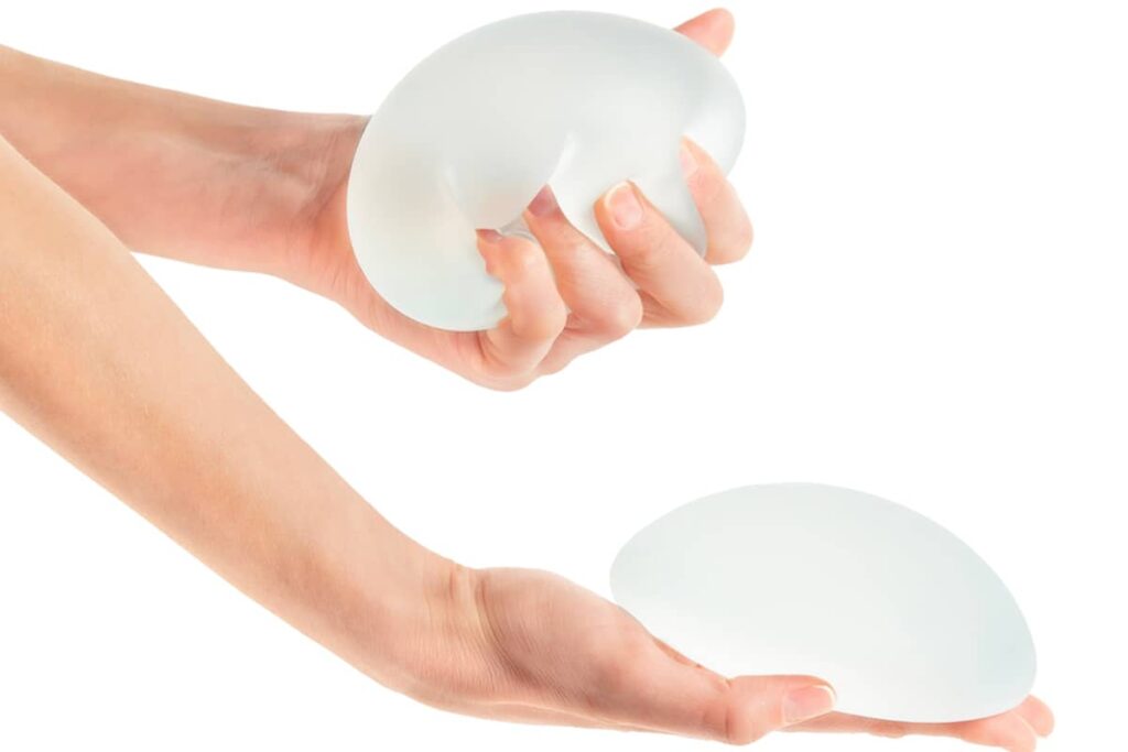 A person’s hands holding two cohesive silicone gel breast implants against a white background, demonstrating their shape and texture.