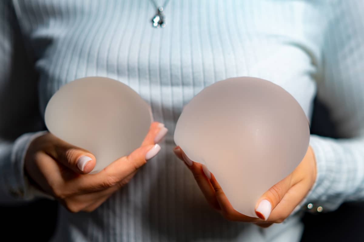 A close-up of a woman in a ribbed sweater holding two silicone breast implants in her hands.