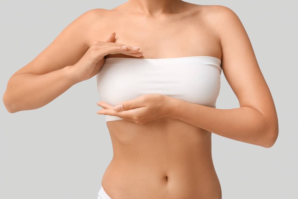 A woman in a white tube top placing her hands over her breasts to examine the healing progress and skin texture after a breast lift procedure.