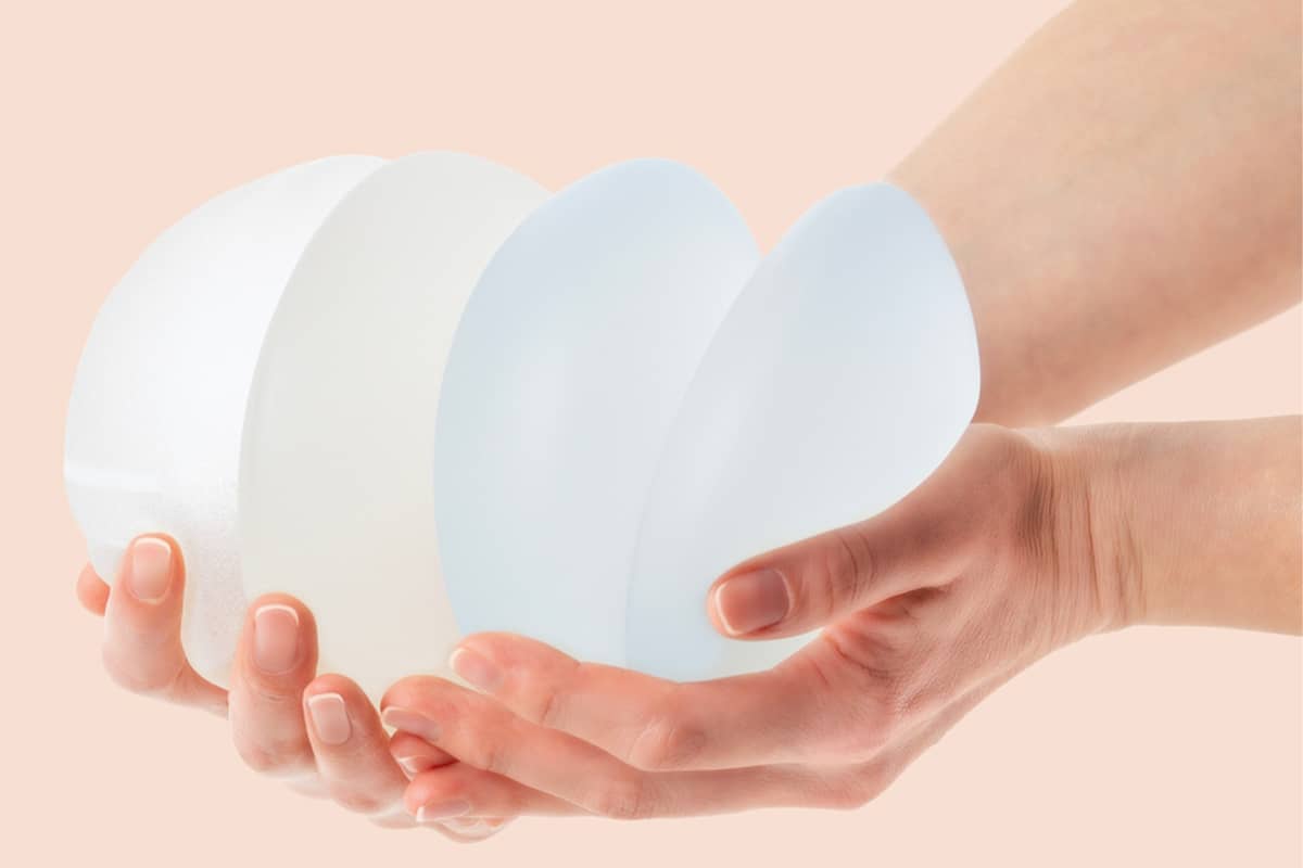 A person's hands holding four different silicone breast implants fanned out to show various sizes and profiles.