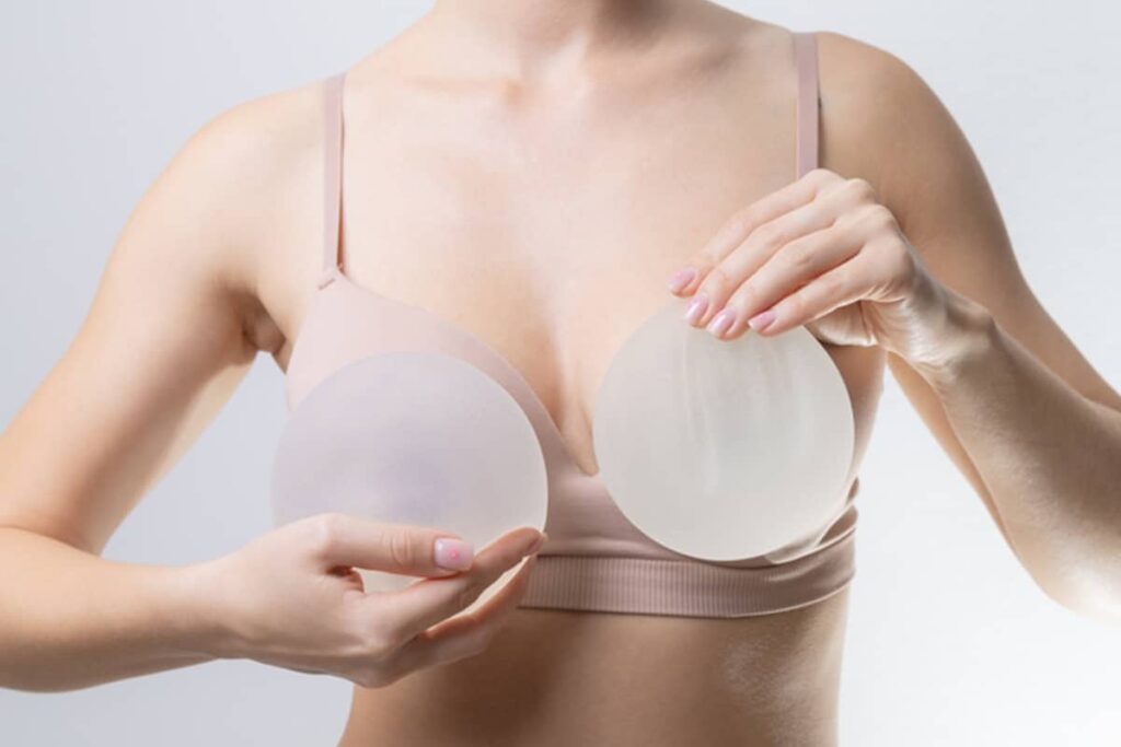 A woman holding two identical frosted silicone implants in front of her chest to demonstrate symmetry and size options.