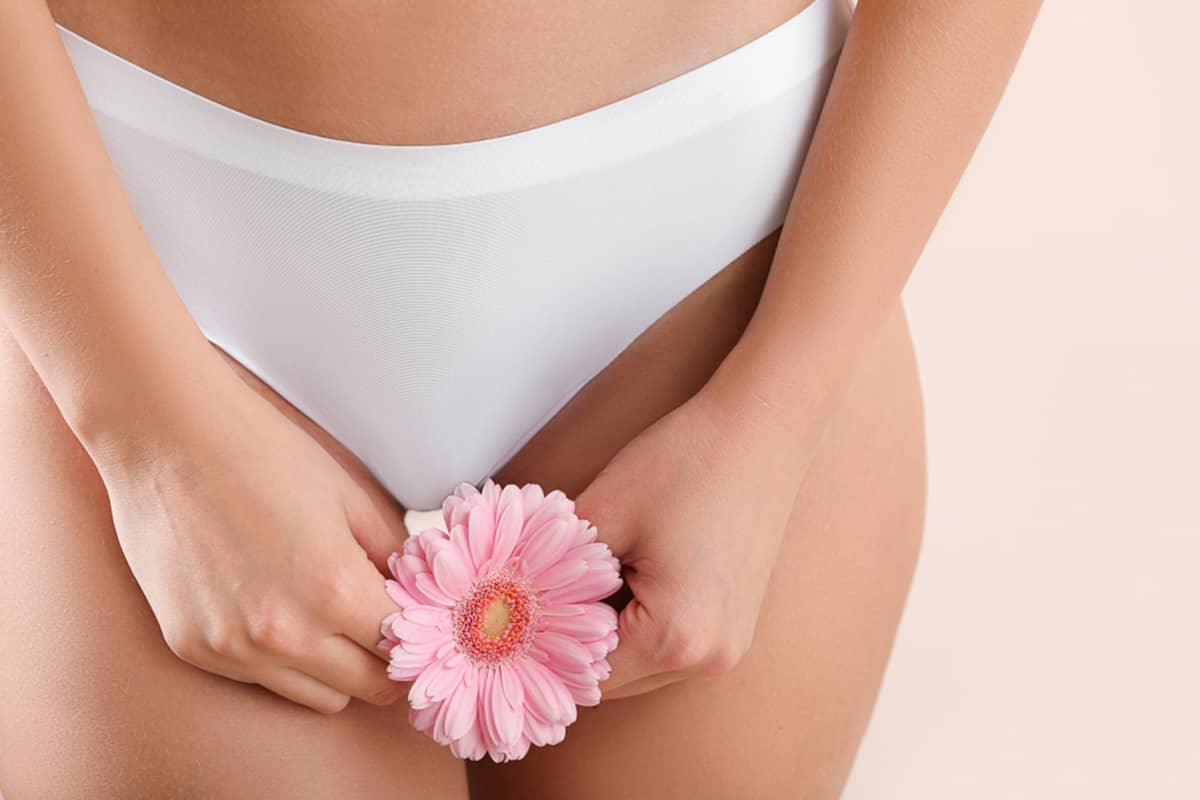 A woman in white lingerie holding a pink flower, symbolizing the delicate nature of intimate health and the importance of preserving sensation during labiaplasty.