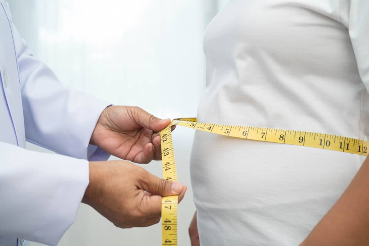 A medical professional using a yellow measuring tape to assess a patient’s midsection circumference during a body contouring consultation.