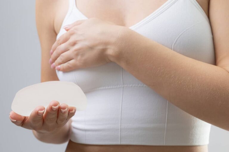 A woman in a white sports bra performs a self-exam while holding a silicone breast implant for comparison.