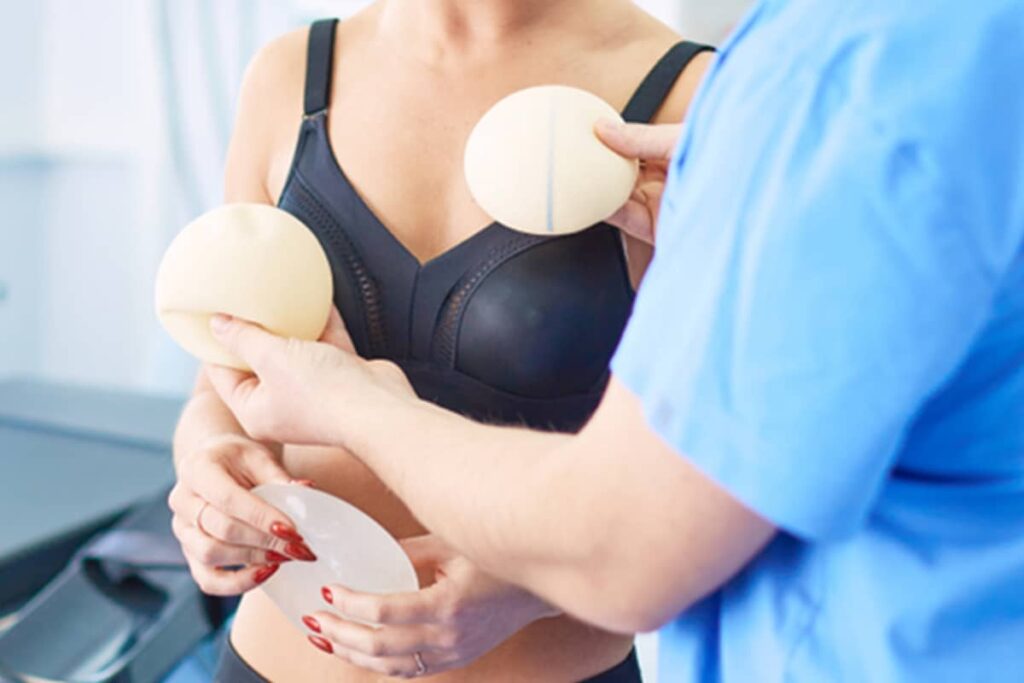 A plastic surgeon in a white coat discusses breast implant options with a patient, holding a silicone implant during a clinical consultation.
